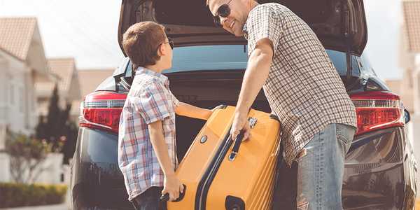 A father and son placing a travelling bag in a car.